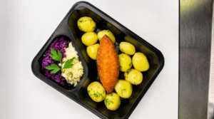 Pierszkurczakazbekonemisosemgdynia Ready to eat tray meal crispy breaded fish fillet with dill seasoned new potatoes and a side of purple cabbage and mashed potatoes with parsley