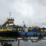 Yellow dredging vessel nosorożec s 05 on a blue barge at a harbor with a crane and other equipment in the background